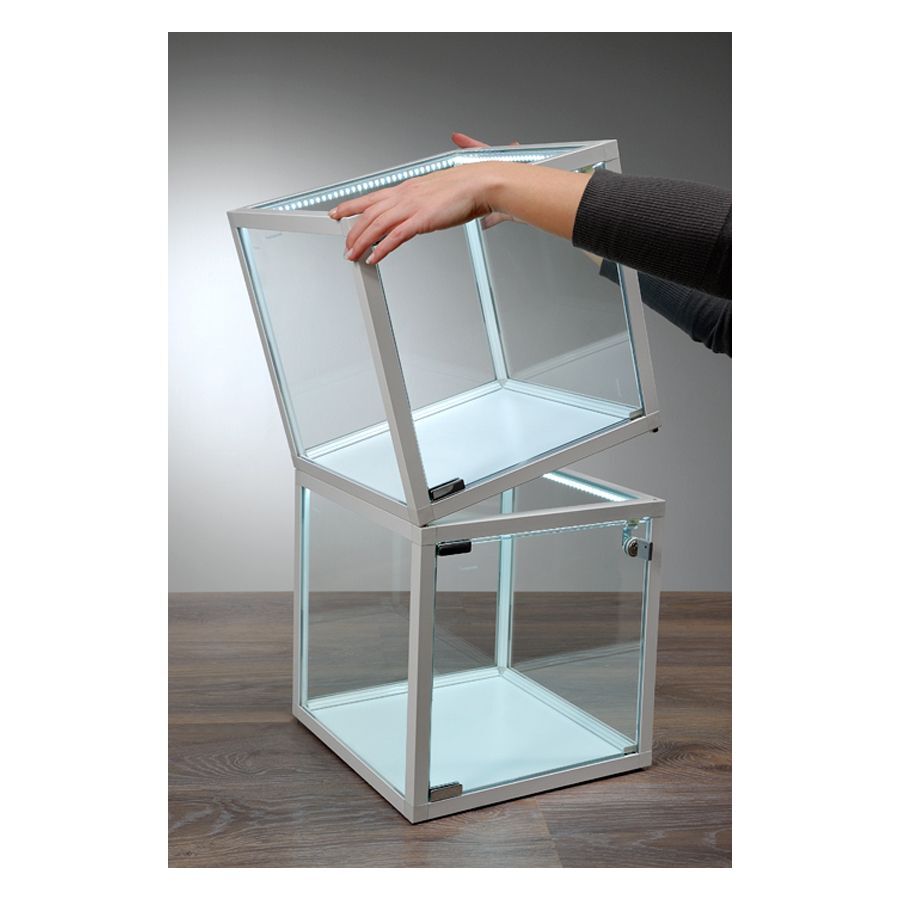 Cube vitrine blanc avec éclairage LED Deux cubes vitrines en verre blanc avec bandes LED sur une table en bois, une main soulève le cube supérieur