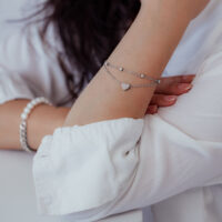 Bracelet à deux rangs en argent avec pendentif cœur au poignet d'une personne en vêtements blancs