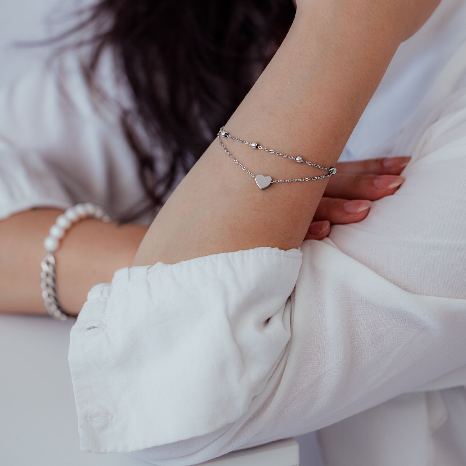 Bracelet à deux rangs en argent avec pendentif cœur au poignet d'une personne en vêtements blancs
