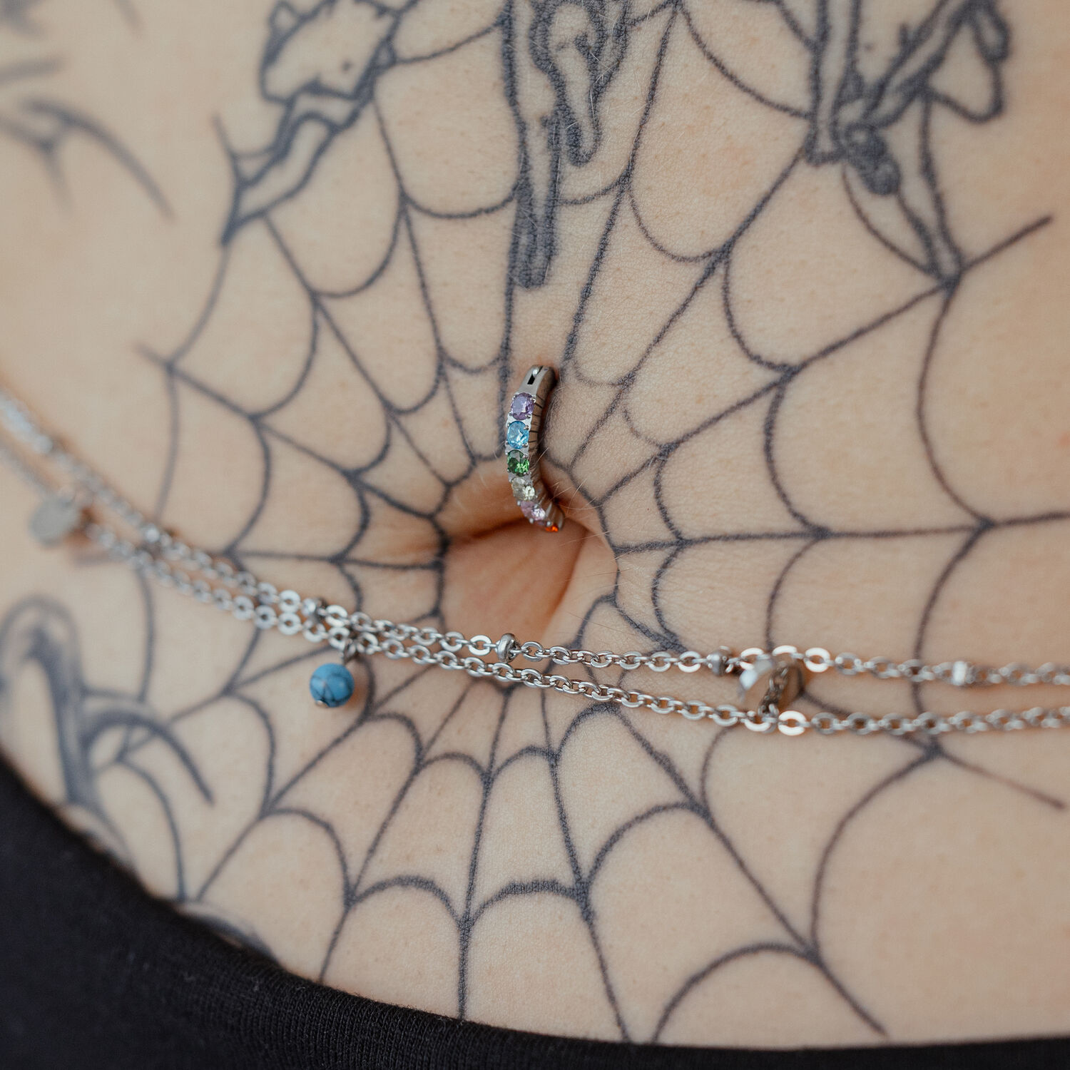 Piercing de nombril avec cristaux arc-en-ciel sur peau tatouée, gros plan