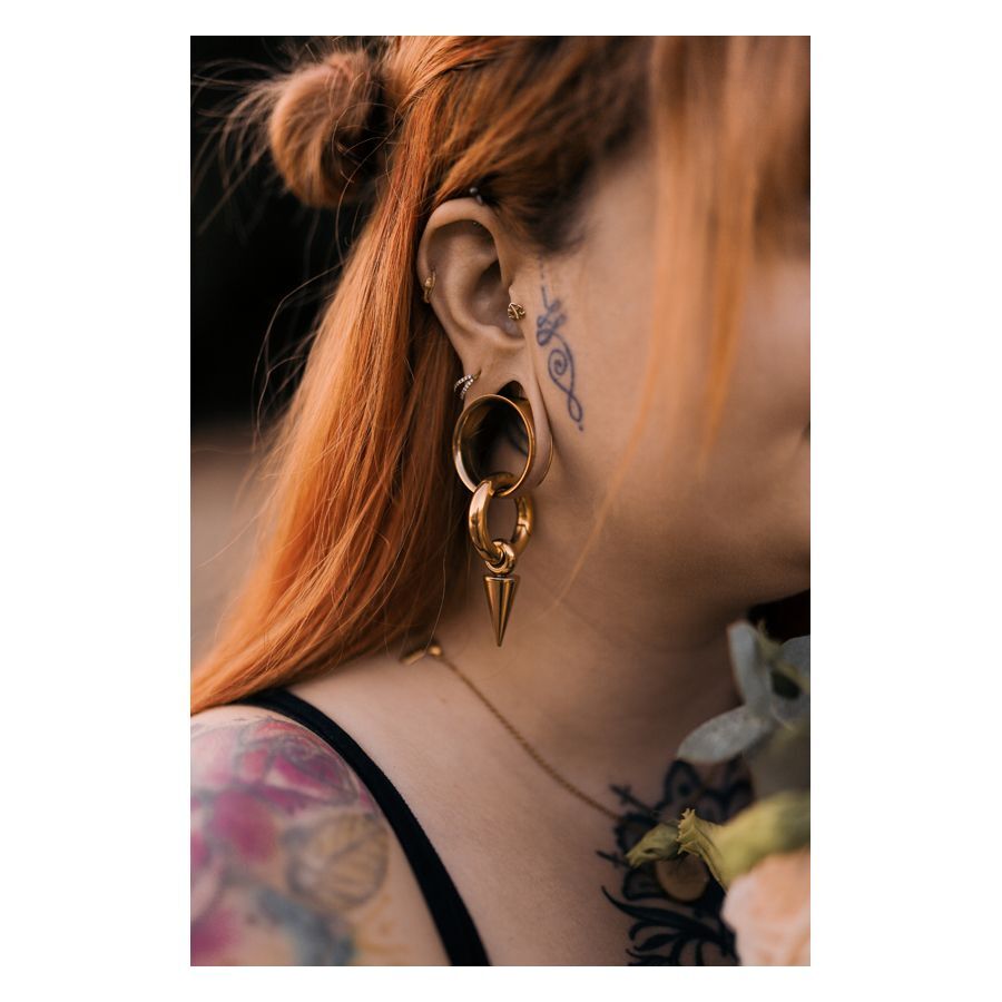 Femme aux cheveux rouges portant un Labret Push-Fit Monstera doré à l'oreille, tatouages visibles