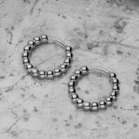 Boucles d'oreilles Bubble Hoops argentées sur fond de béton Deux boucles d'oreilles Bubble Hoops argentées en acier inoxydable sur fond de béton gris