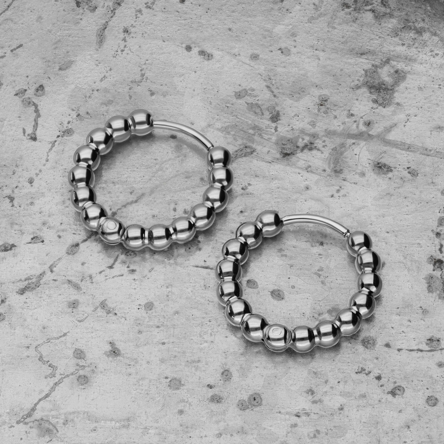 Boucles d'oreilles Bubble Hoops argentées sur fond de béton Deux boucles d'oreilles Bubble Hoops argentées en acier inoxydable sur fond de béton gris
