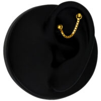 Chaîne de piercing en or 14K sur oreille noire Chaîne de piercing en or 585 sur une oreille noire sur fond noir
