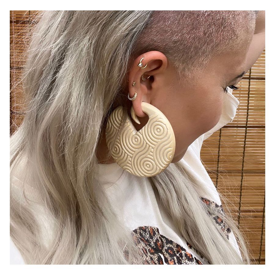 Grands poids d'oreille en bois beige Poids d'oreille en bois beige avec motif circulaire à l'oreille d'une personne devant un fond de bambou