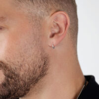 Créoles argentées à l'oreille d'un homme Créoles argentées à l'oreille d'un homme avec barbe sur fond blanc