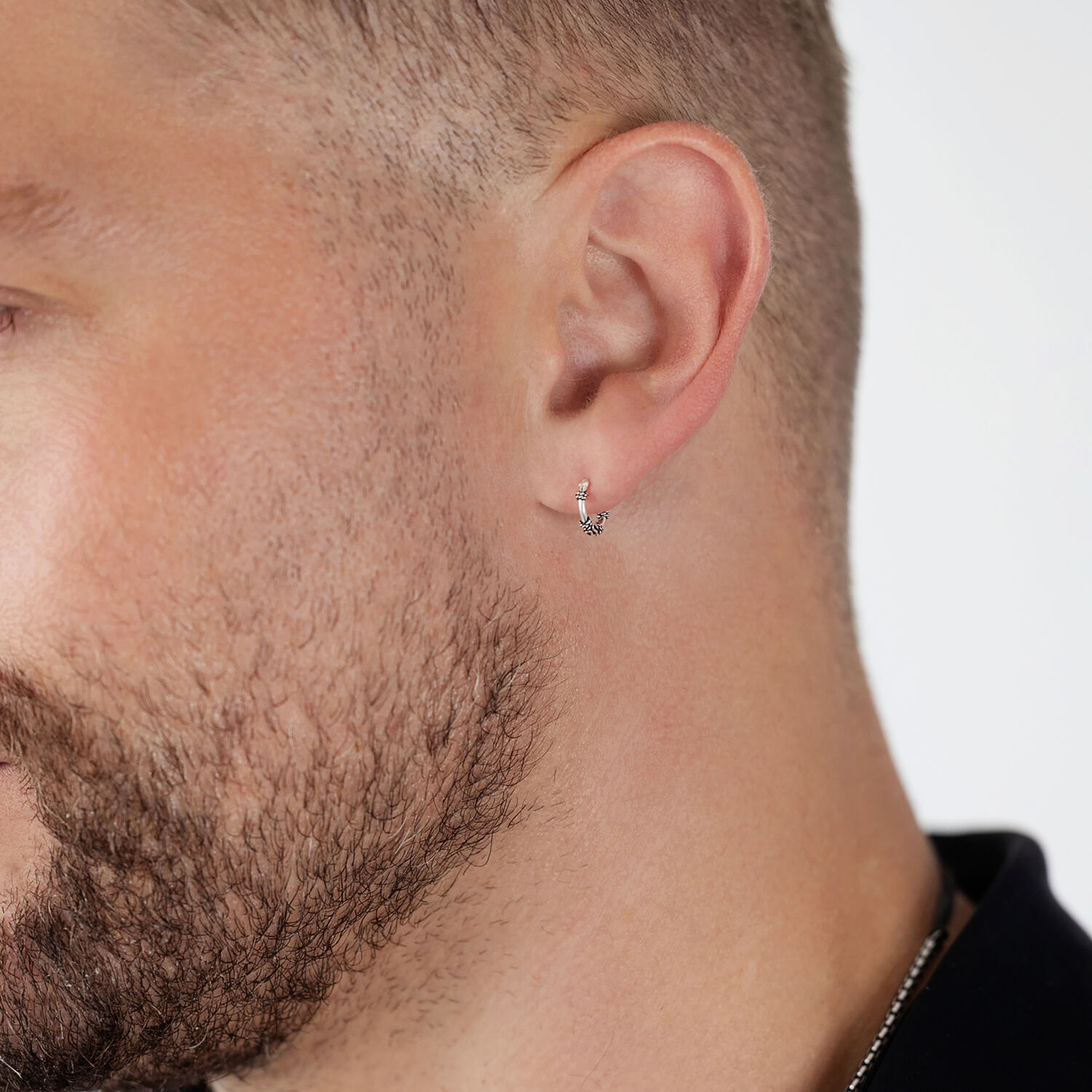 Créoles argentées à l'oreille d'un homme Créoles argentées à l'oreille d'un homme avec barbe sur fond blanc