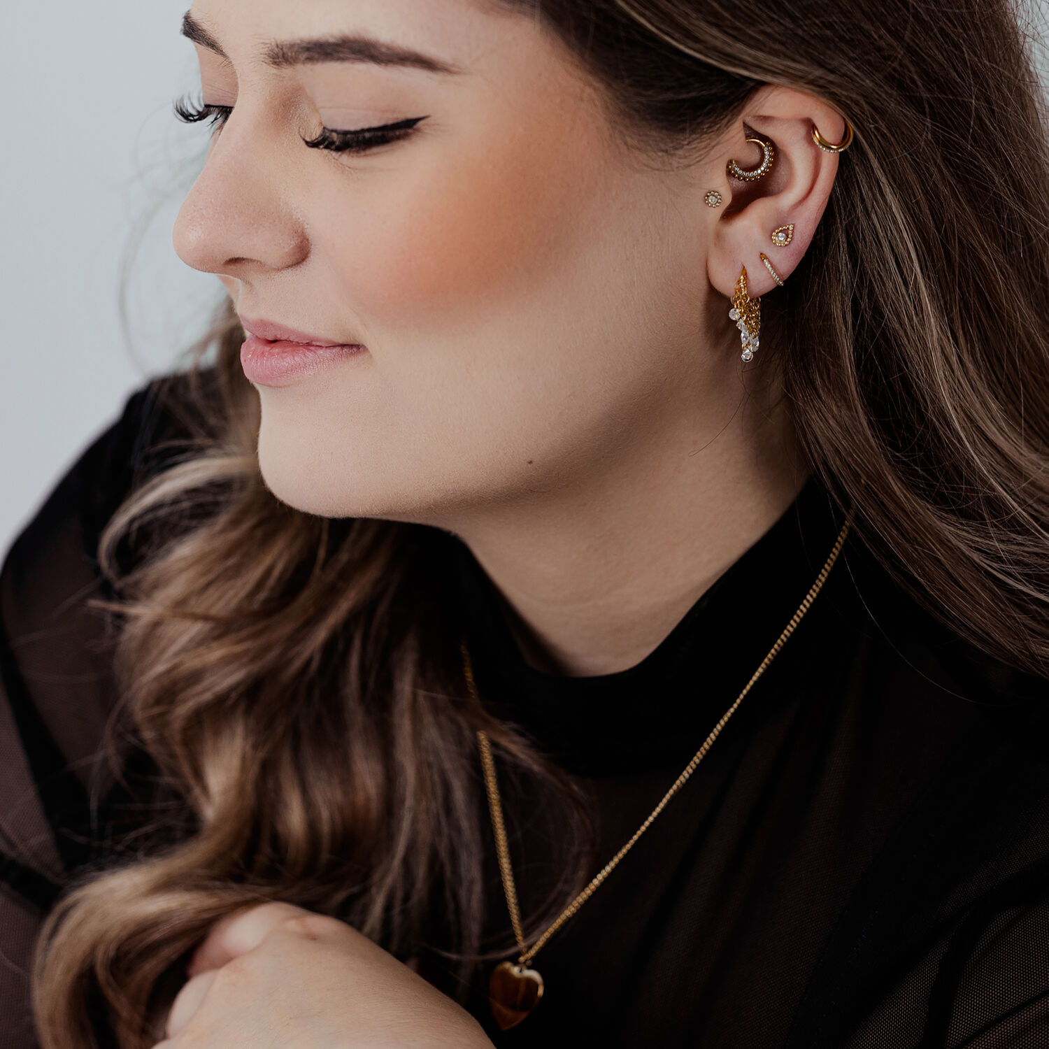 Femme avec des anneaux de piercing en or et des cristaux à l'oreille sur fond clair