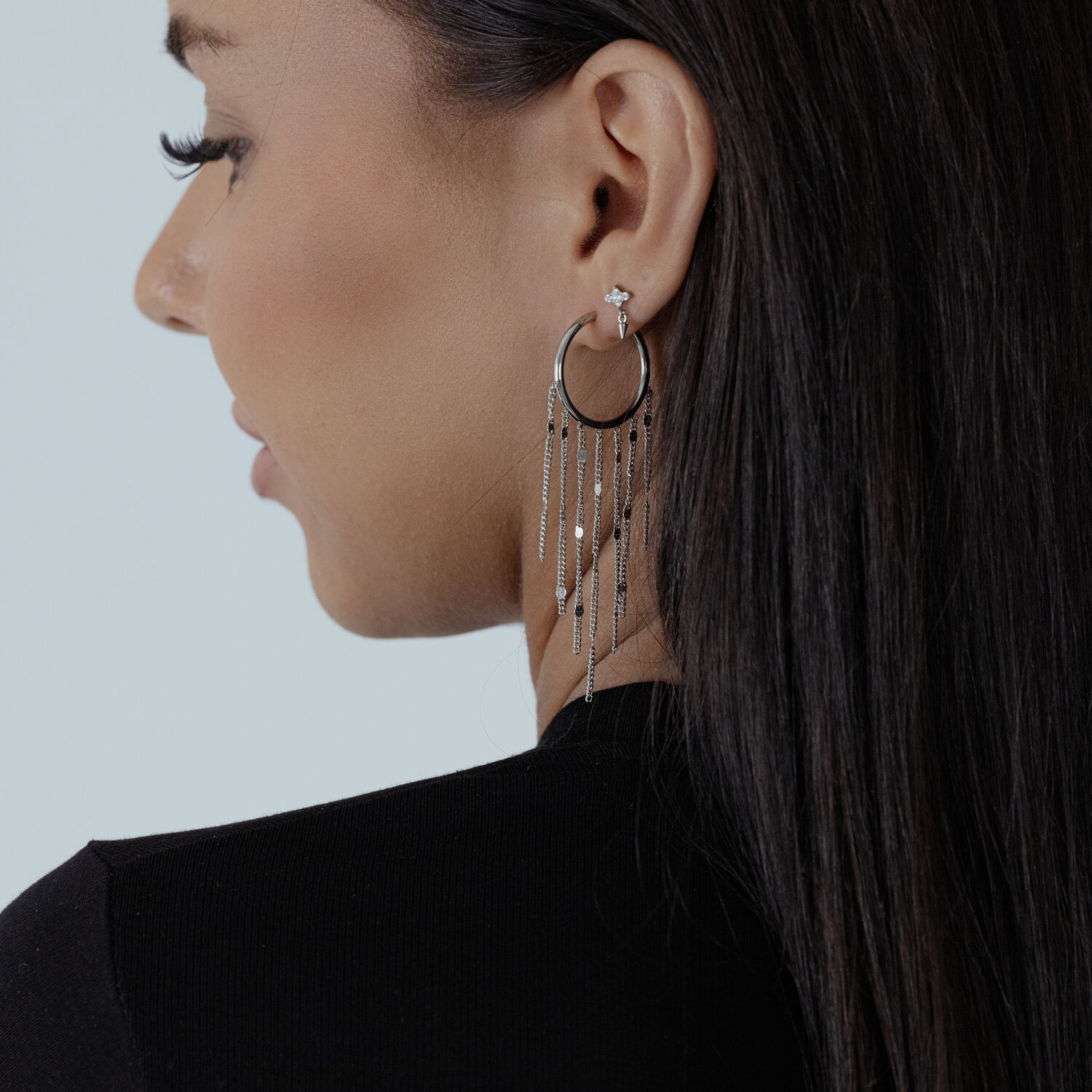 Boucles d'oreilles élégantes avec pompons noirs et argentés Femme aux longs cheveux foncés portant des boucles d'oreilles à pompons noirs et argentés sur fond blanc