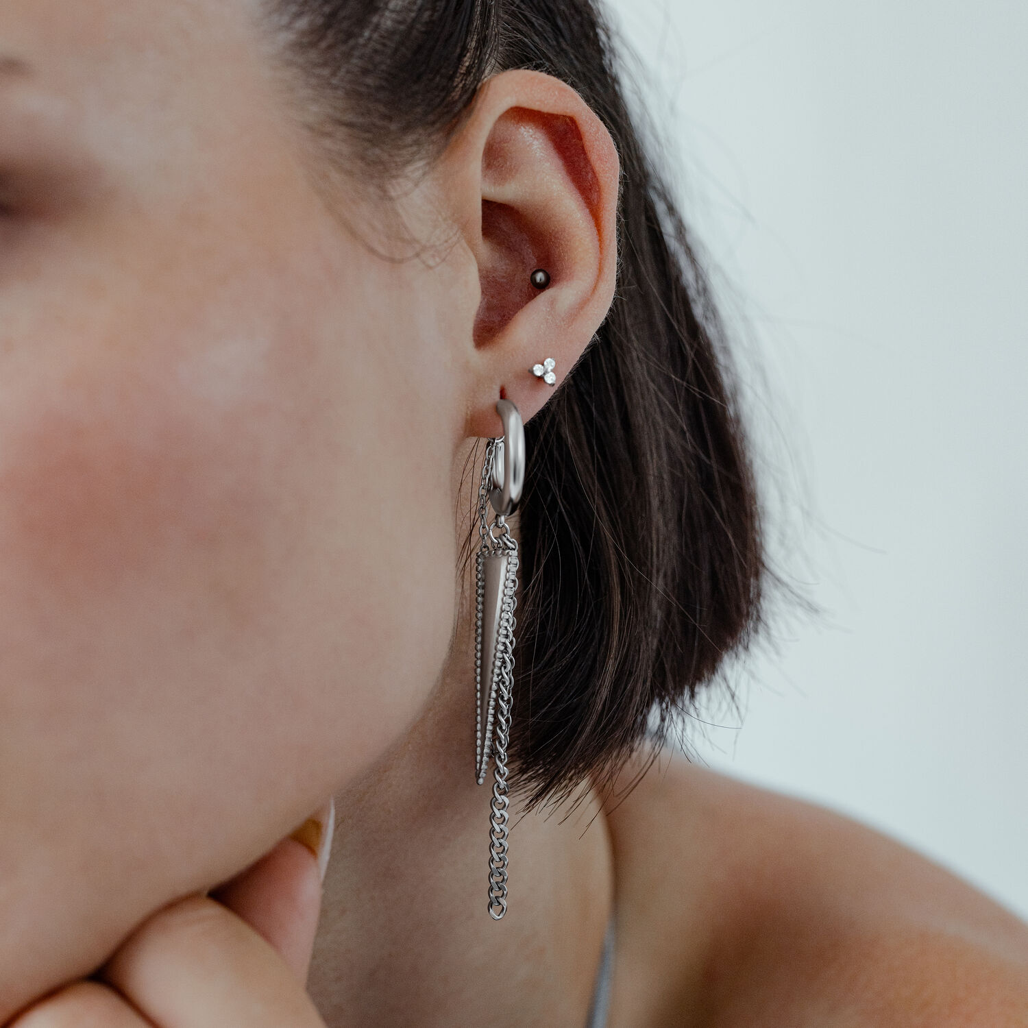 Boucles d'oreilles triangle argentées à l'oreille Boucles d'oreilles triangle argentées à l'oreille d'une femme aux cheveux courts sur fond clair