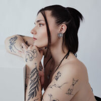 Élégants clous d'oreilles fleur en acier inoxydable Portrait latéral d'une personne tatouée avec des clous d'oreilles fleur élégants, fond neutre