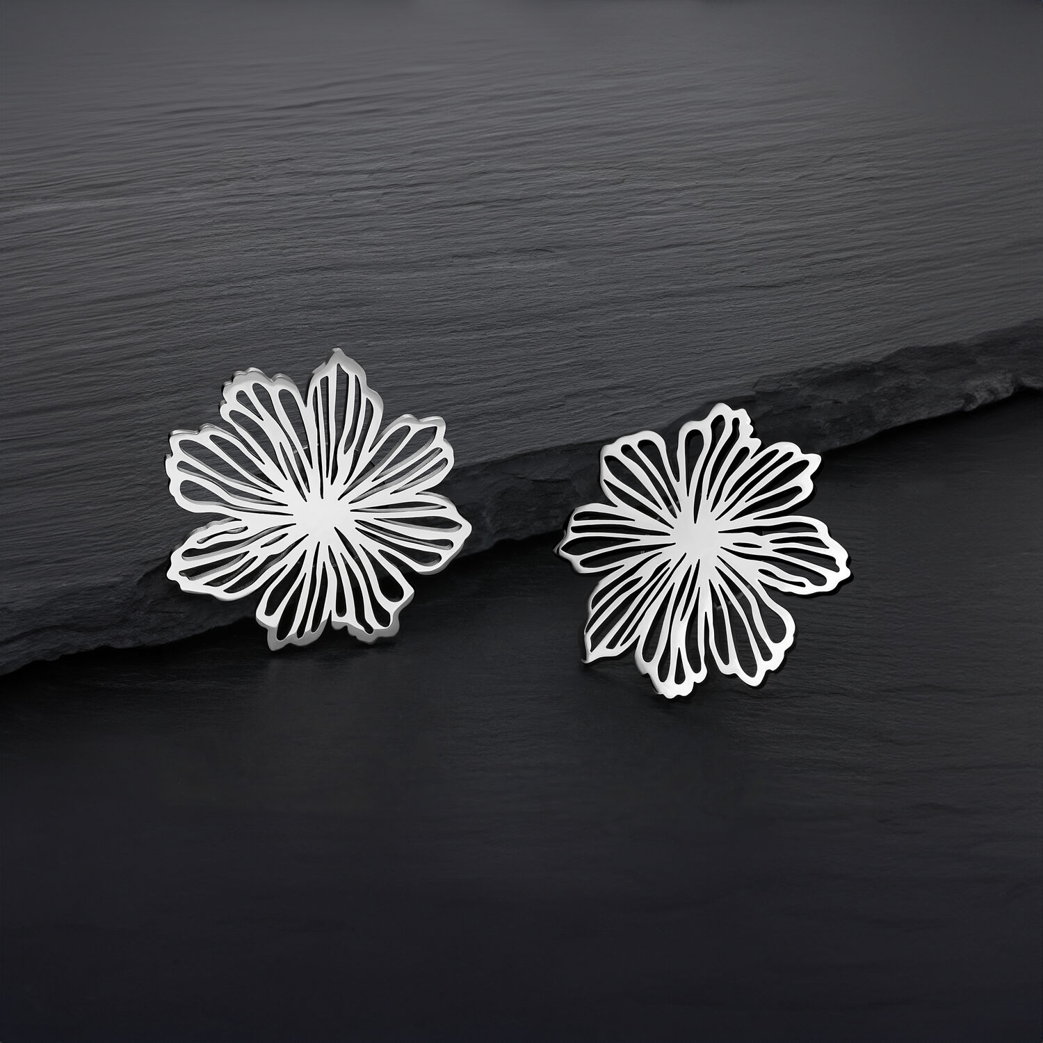 Fins clous d'oreilles fleurs en acier inoxydable Deux clous d'oreilles fleurs en argent en acier inoxydable sur fond sombre