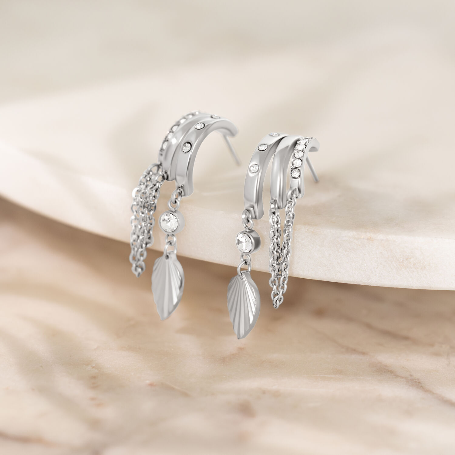 Boucles d'oreilles argentées avec pendentif feuille Boucles d'oreilles argentées avec pierres scintillantes et pendentifs feuilles sur surface en marbre