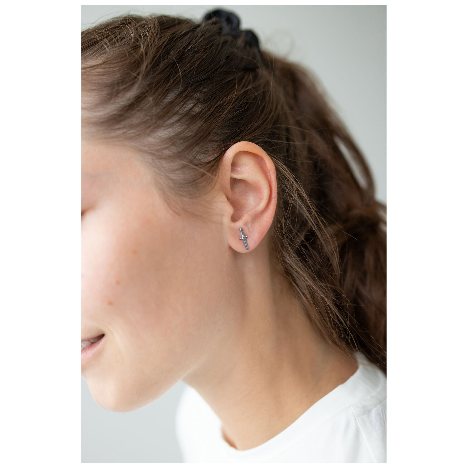 Boucles d'oreilles épée stylées en argent Boucles d'oreilles épée en argent sur l'oreille d'une femme devant un fond clair