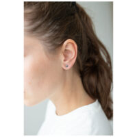 Boucles d'oreilles cœur argentées sur l'oreille d'une femme aux cheveux bruns, fond blanc