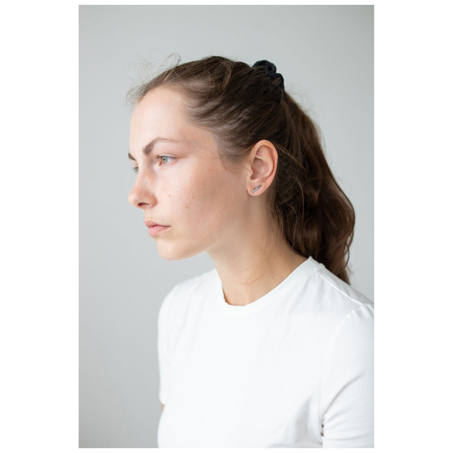 Boucles d'oreilles élégantes en acier inoxydable Femme aux cheveux bruns portant des boucles d'oreilles discrètes en argent sur fond gris