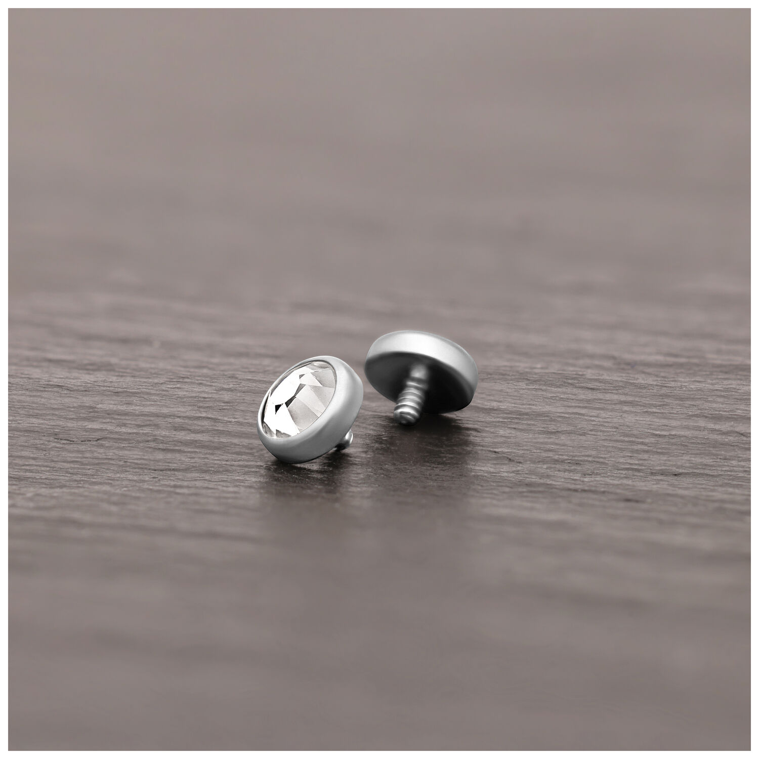 Embout de piercing en titane argenté avec cristal Embout de piercing en titane argenté avec cristal clair sur surface en bois