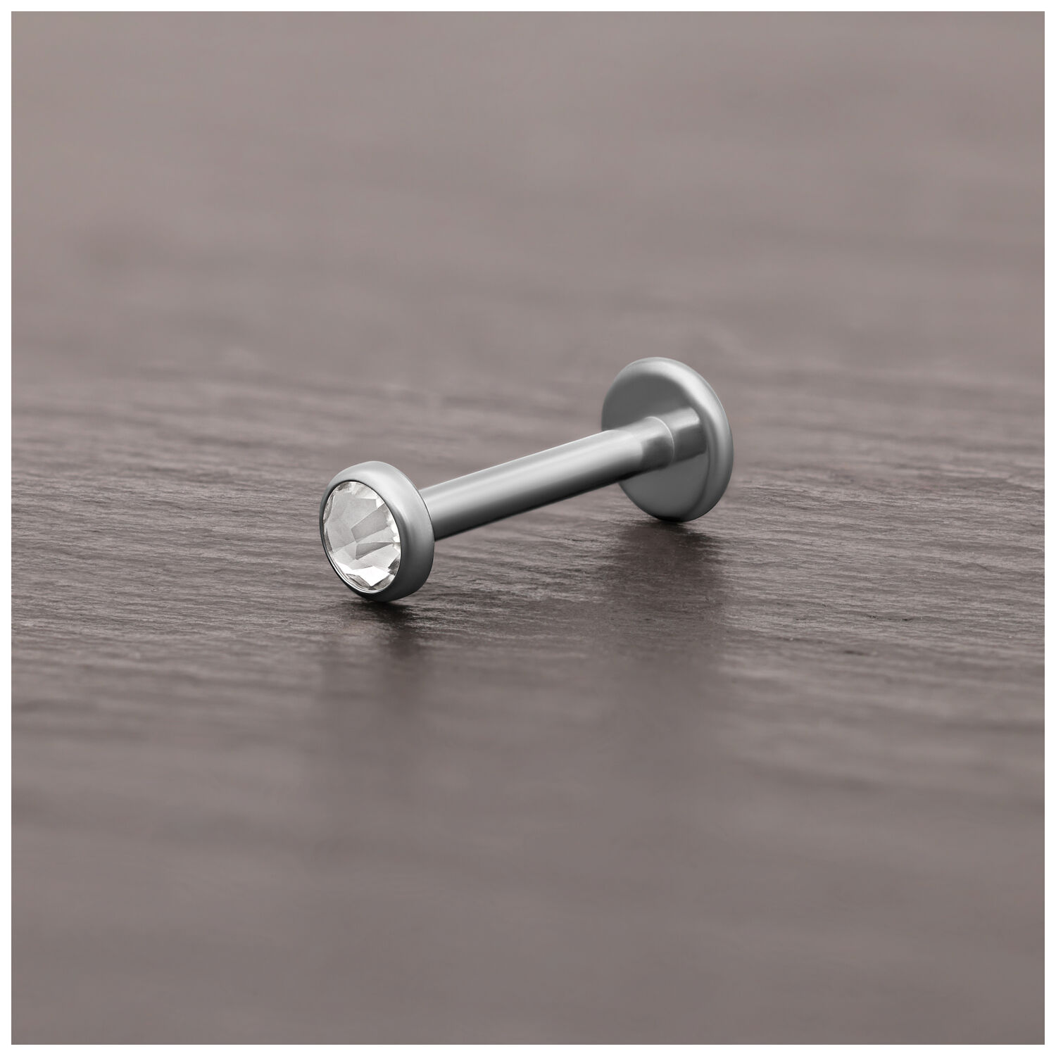 Embout de piercing en titane argenté avec cristal Embout de piercing en titane argenté avec cristal clair sur surface en bois sombre