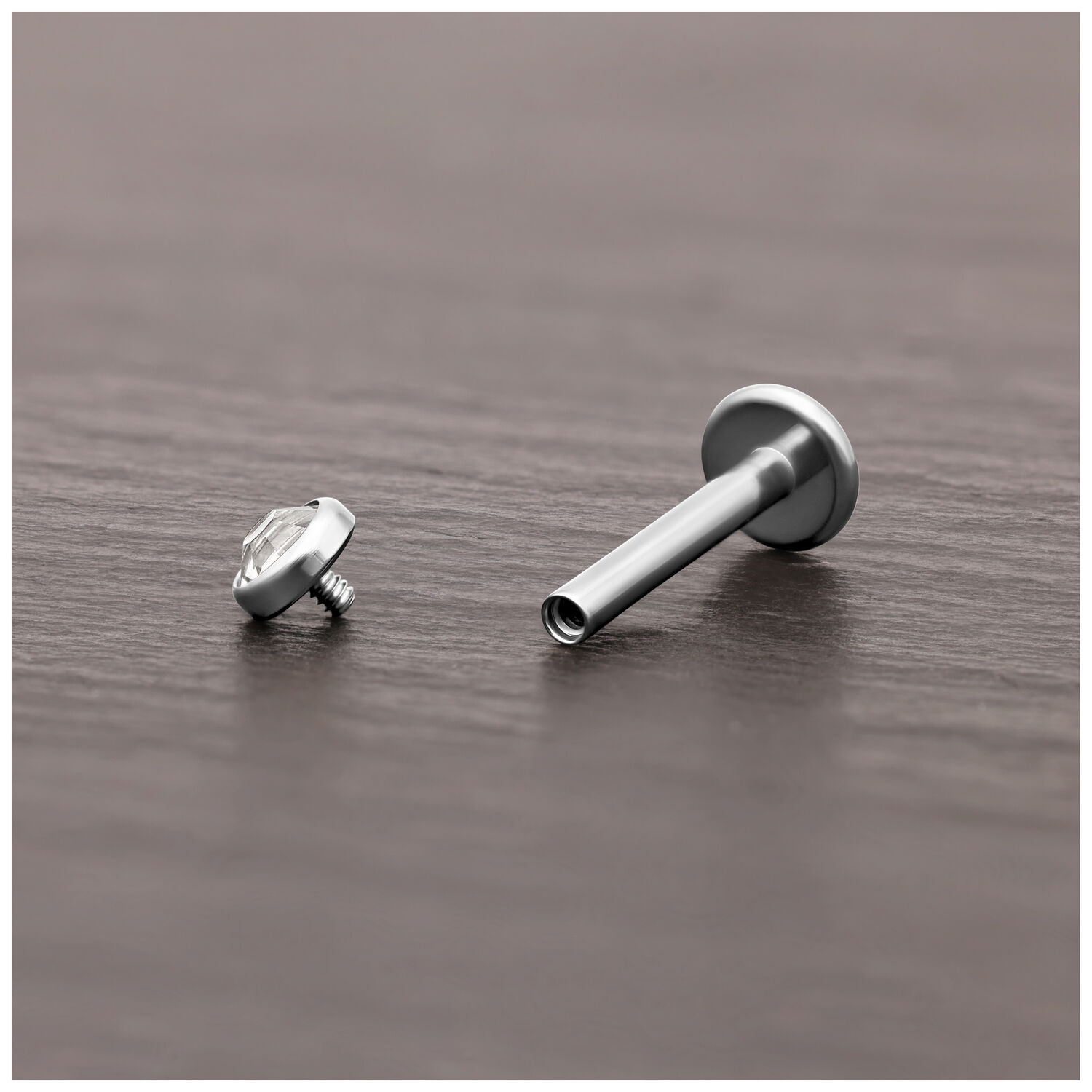 Embout de piercing en titane avec cristal Embout de piercing en titane argenté avec cristal clair sur bois sombre.