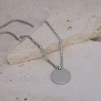 Chaîne argentée avec pendentif rond Chaîne argentée avec pendentif rond sur sol en pierre claire