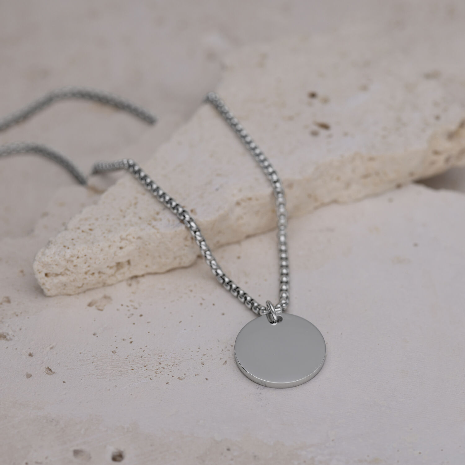 Chaîne argentée avec pendentif rond Chaîne argentée avec pendentif rond sur sol en pierre claire