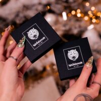 Ensemble de bijoux cœur dans une boîte cadeau noire Deux boîtes cadeaux noires avec logo Wildcat, tenues par des mains aux ongles dorés