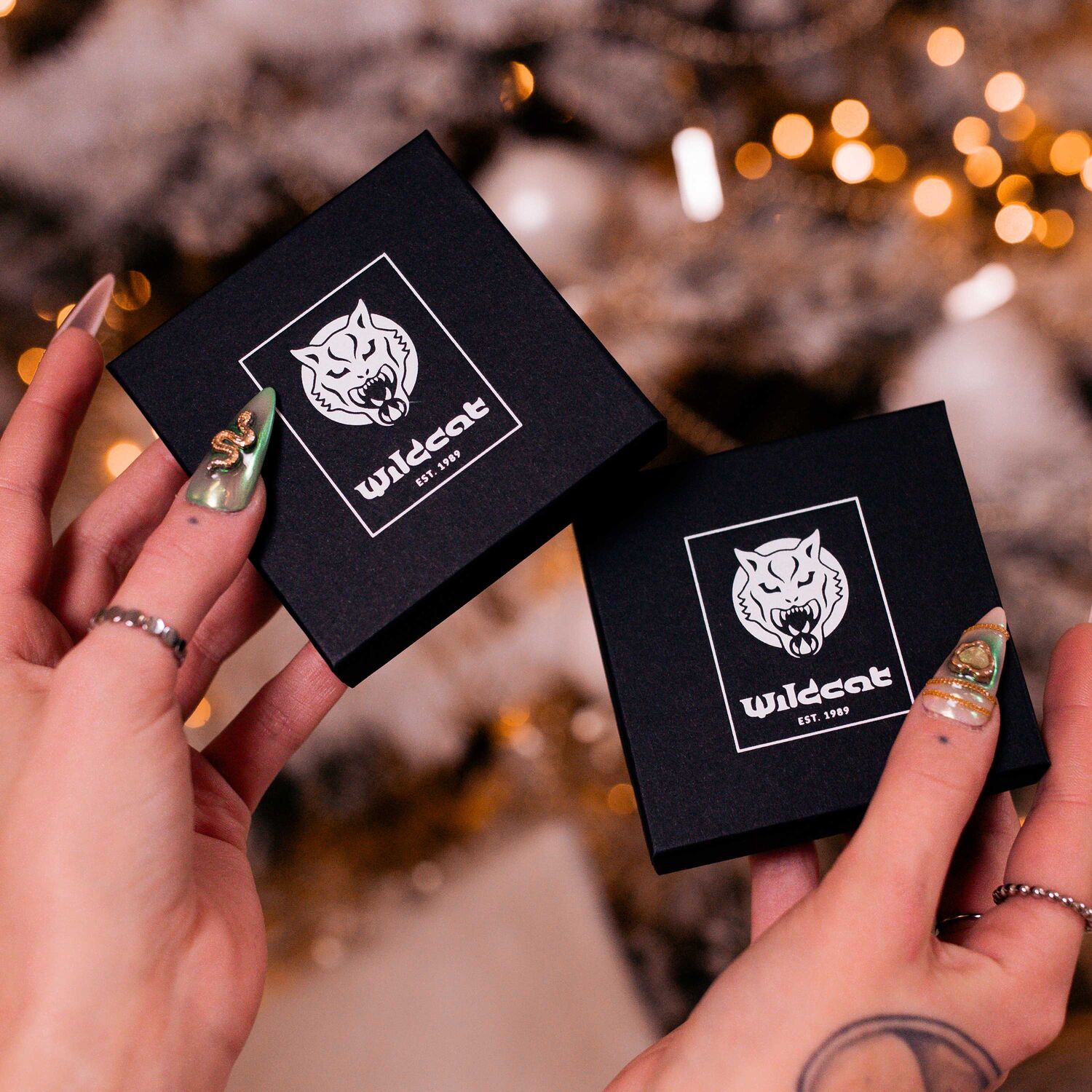 Ensemble de bijoux cœur dans une boîte cadeau noire Deux boîtes cadeaux noires avec logo Wildcat, tenues par des mains aux ongles dorés