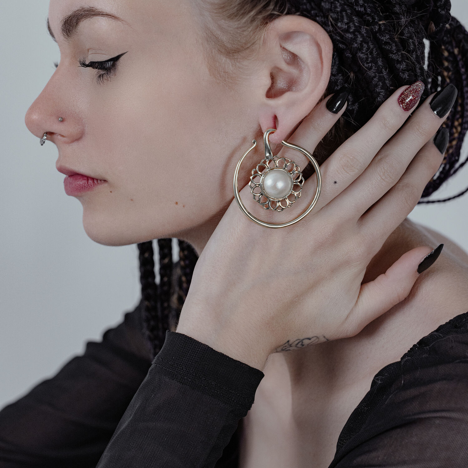 Poids d'oreilles Golden Whirl White Onyx de Wildcat Femme avec une tresse, portant de grands poids d'oreilles dorés avec onyx blanc, main à l'oreille