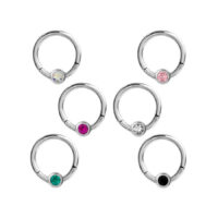 Cinq clickers de septum argentés avec des cristaux de différentes couleurs sur fond blanc