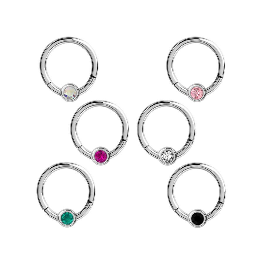 Cinq clickers de septum argentés avec des cristaux de différentes couleurs sur fond blanc