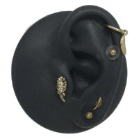 Disque en silicone pour piercing avec embouts dorés Modèle d'oreille en silicone noir avec embouts de piercing dorés sur fond blanc