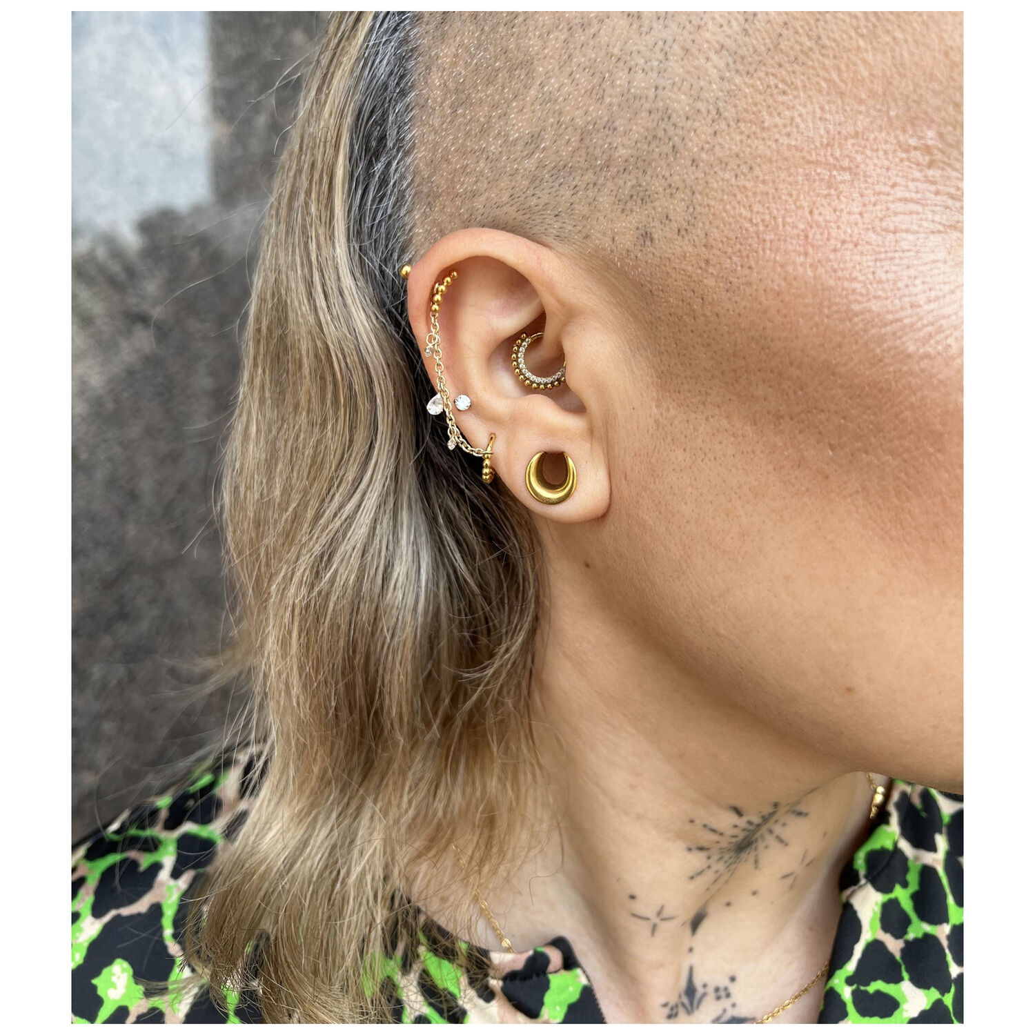 Gros plan d'une oreille avec plusieurs anneaux de piercing en or et cristaux