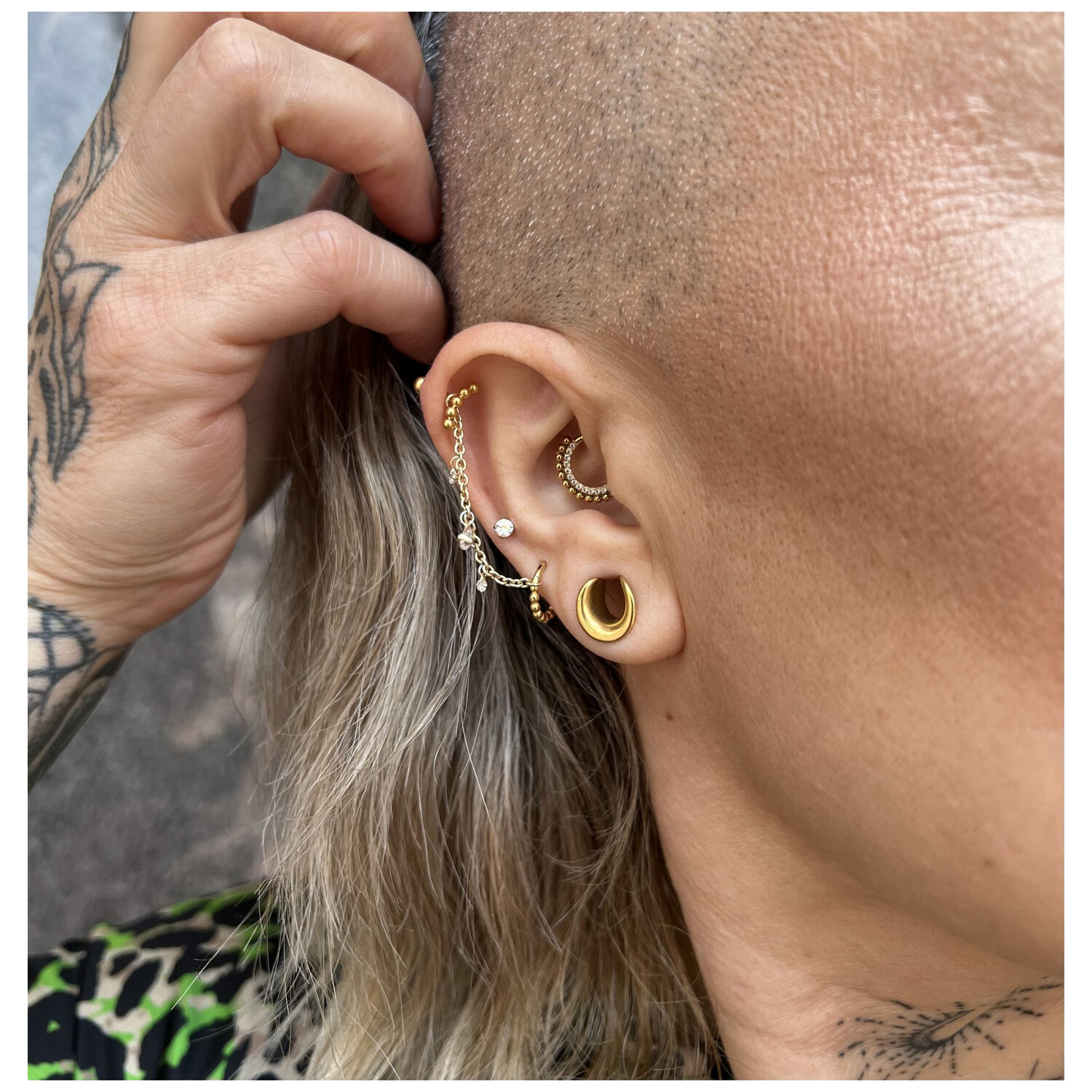 Anneau de piercing doré avec petites boules de cristal sur une oreille avec plusieurs piercings.