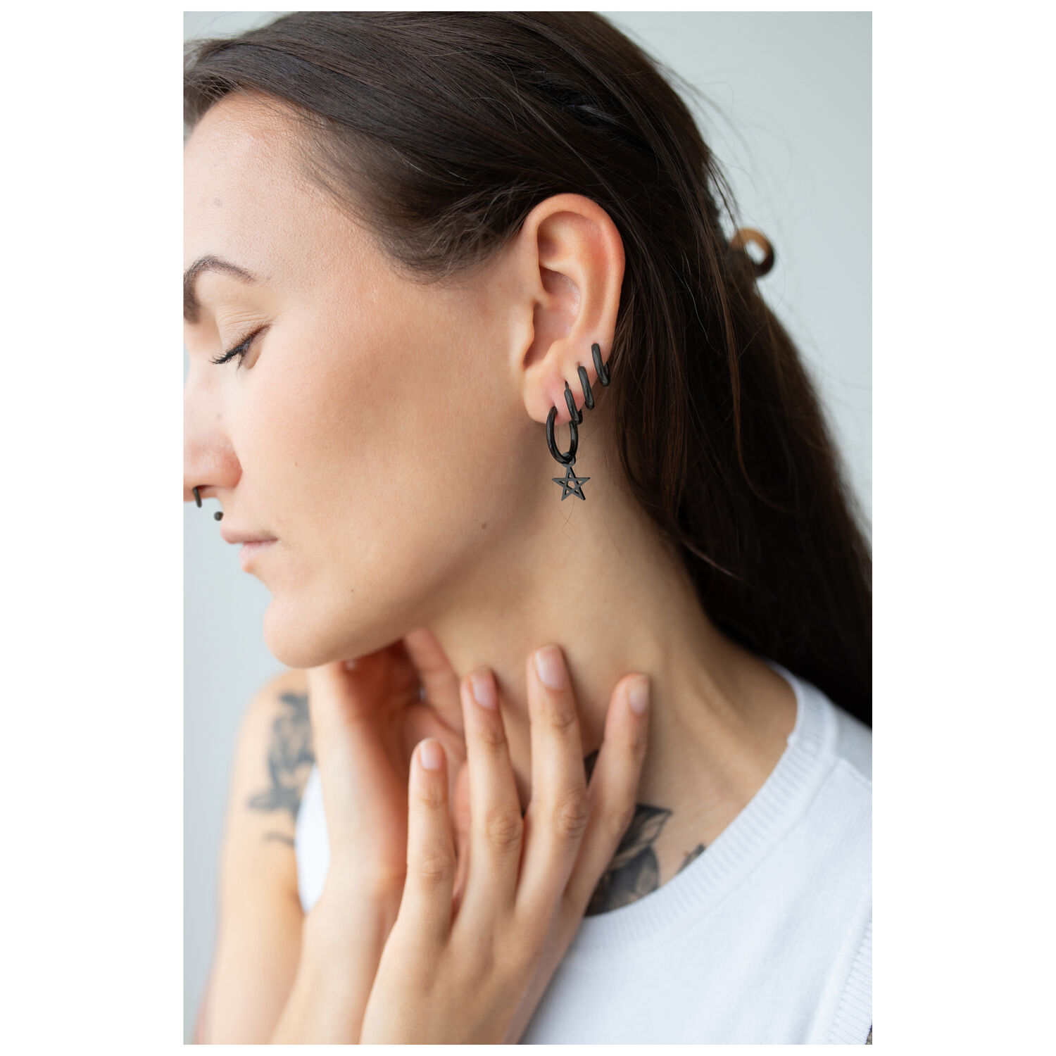 Créoles pentagramme noires en acier inoxydable Femme avec des boucles d'oreilles pentagramme noires en acier inoxydable sur fond clair
