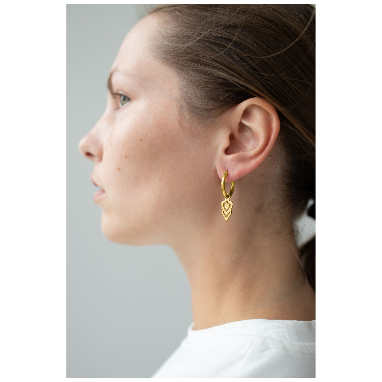 Petits anneaux Balisuta dorés en profil Femme avec des petits anneaux Balisuta dorés devant un fond neutre