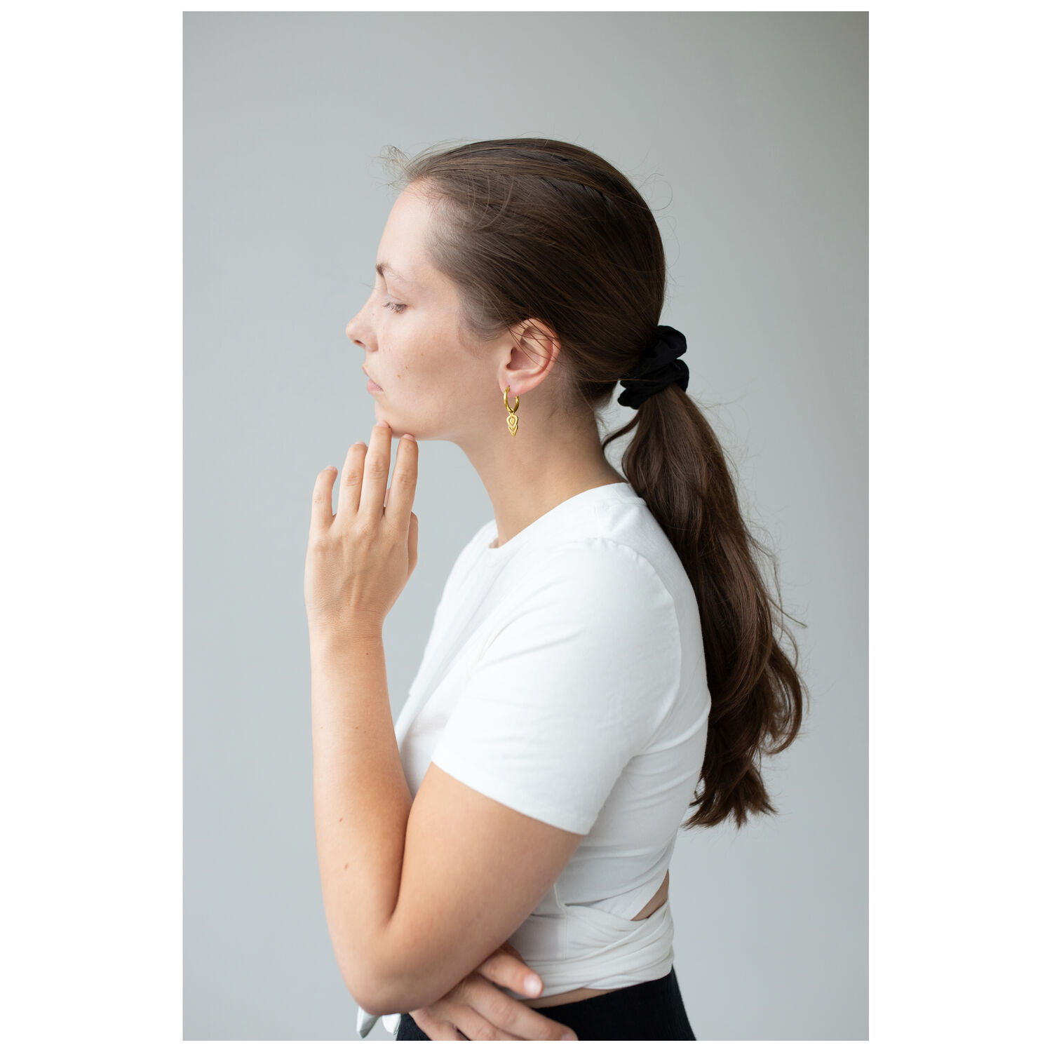 Boucles d'oreilles Little Balisuta Hoops dorées Femme aux cheveux longs portant des boucles d'oreilles hoops dorées sur fond gris