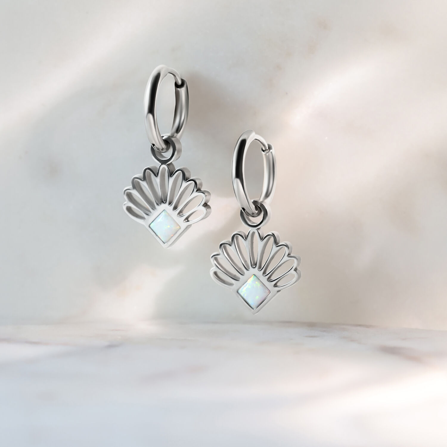 Boucles d'oreilles en opale argentée sur fond de marbre Boucles d'oreilles en éventail d'opale argentée sur fond de marbre clair, haute brillance