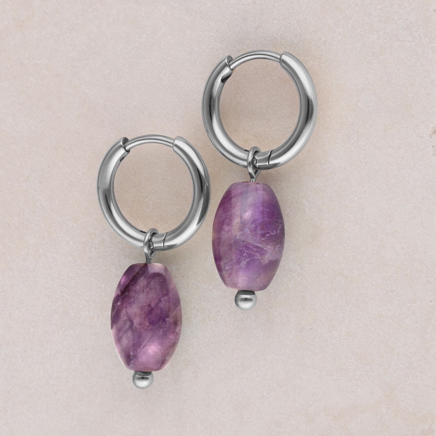 Créoles argentées avec pendentif améthyste Deux créoles argentées avec pendentif améthyste violet sur fond beige