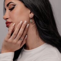 Créoles en aventurine verte portées par une femme Femme aux longs cheveux noirs portant des boucles d'oreilles en aventurine verte et un pull blanc
