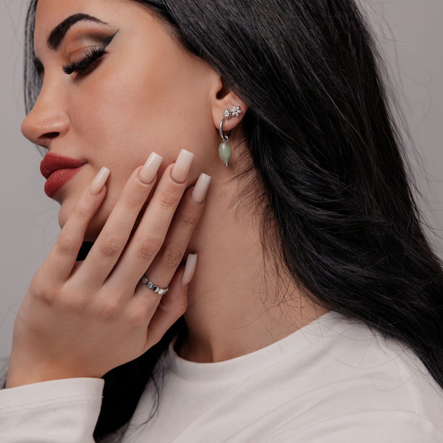 Créoles en aventurine verte portées par une femme Femme aux longs cheveux noirs portant des boucles d'oreilles en aventurine verte et un pull blanc