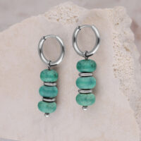Deux créoles argentées avec trois perles turquoise chacune devant une pierre claire