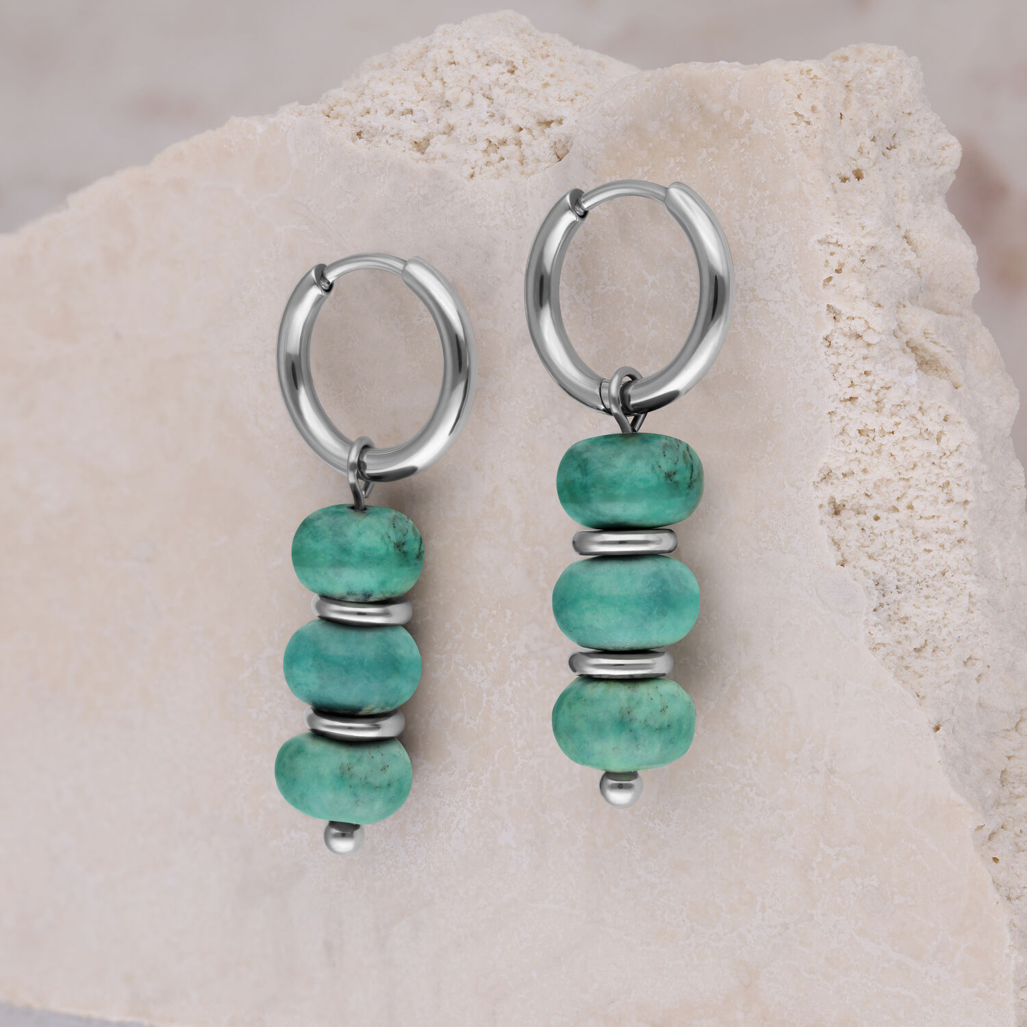 Deux créoles argentées avec trois perles turquoise chacune devant une pierre claire