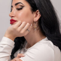 Boucles d'oreilles pendantes élégantes en acier inoxydable argenté Femme aux longs cheveux noirs portant des boucles d'oreilles en acier inoxydable argenté sur fond neutre