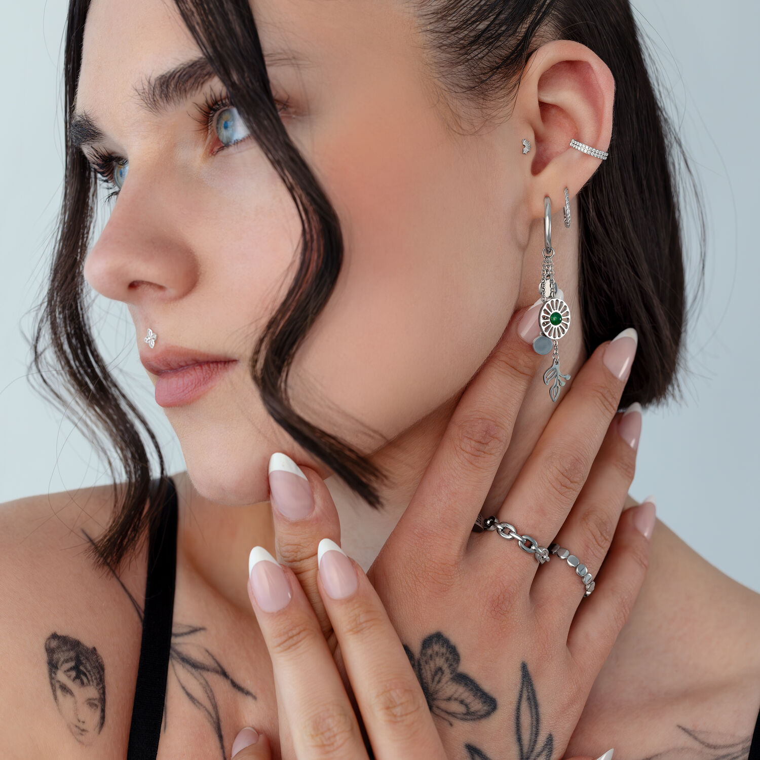 Boucles d'oreilles en argent avec détails en agate mousse Femme avec boucles d'oreilles en argent et agate mousse et tatouages sur fond clair