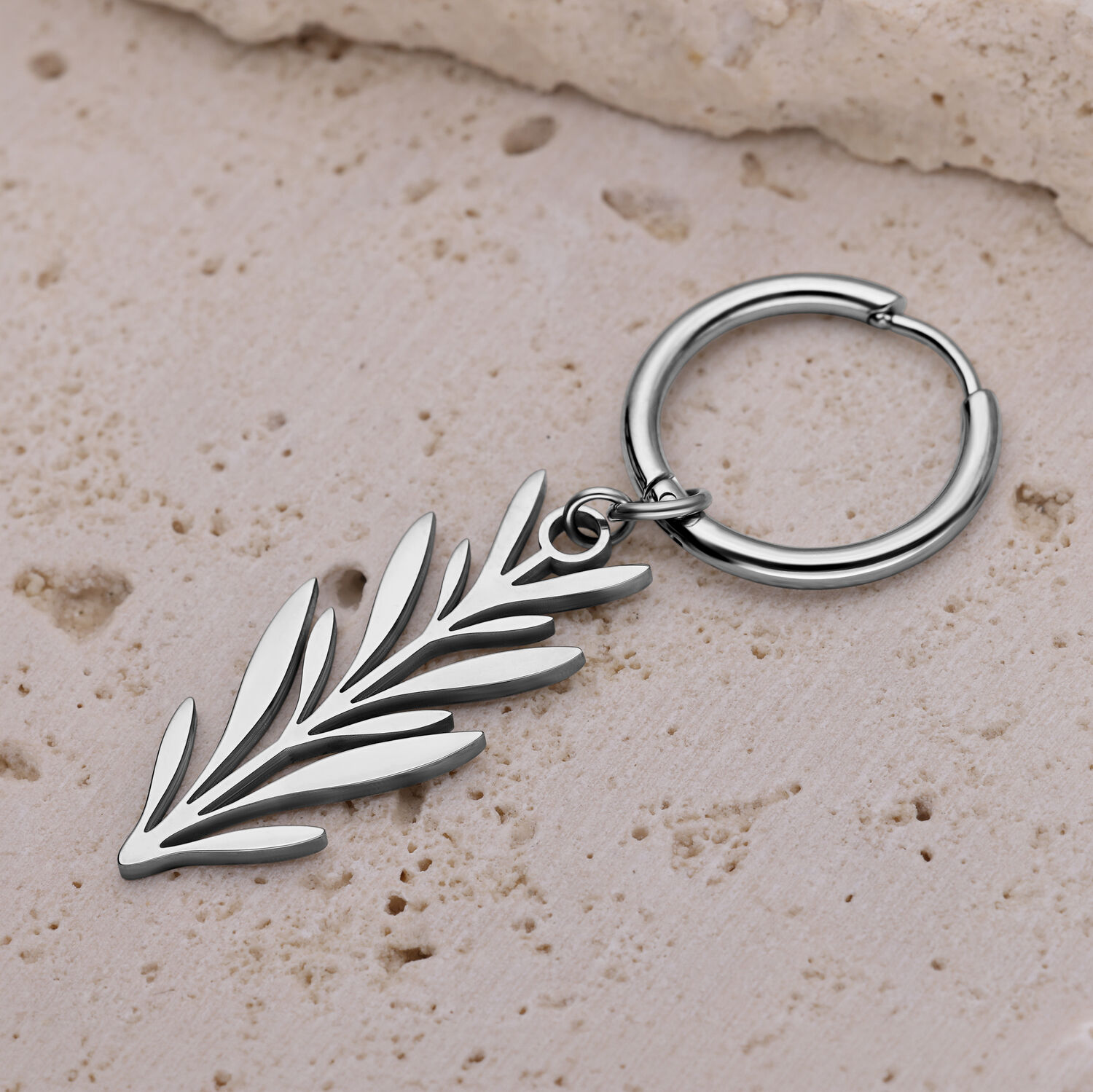Boucle d'oreille en argent avec design de branche Boucle d'oreille en argent avec design de branche sur surface en pierre beige