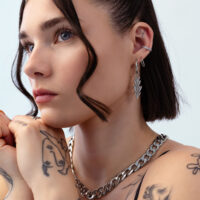 Boucles d'oreilles Lovely Branch argentées à l'oreille Gros plan d'un visage avec des boucles d'oreilles Lovely Branch argentées et des chaînes, sur fond blanc