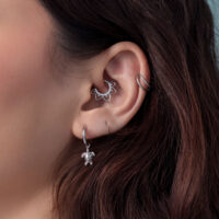 Boucles d'oreilles argentées avec pendentif tortue Gros plan d'une oreille avec des boucles d'oreilles tortue argentées et d'autres piercings, cheveux bruns en arrière-plan