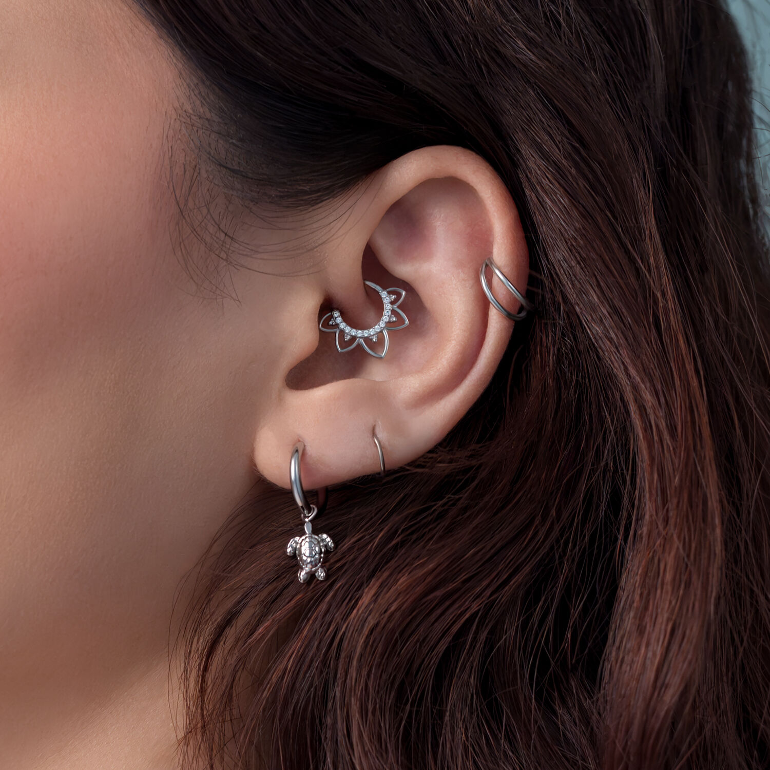 Boucles d'oreilles argentées avec pendentif tortue Gros plan d'une oreille avec des boucles d'oreilles tortue argentées et d'autres piercings, cheveux bruns en arrière-plan