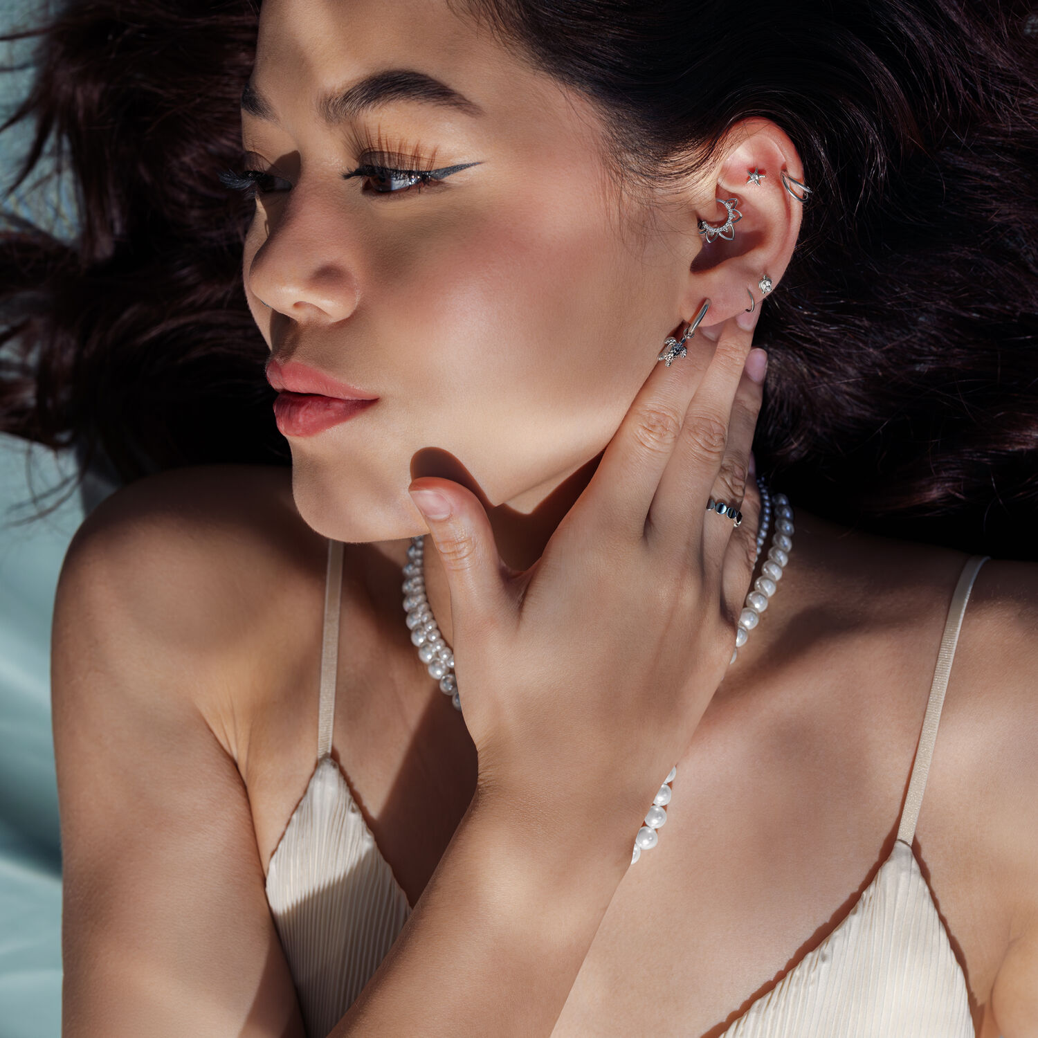Boucles d'oreilles argentées avec collier de perles Femme avec des boucles d'oreilles argentées et un collier de perles, de côté à la lumière