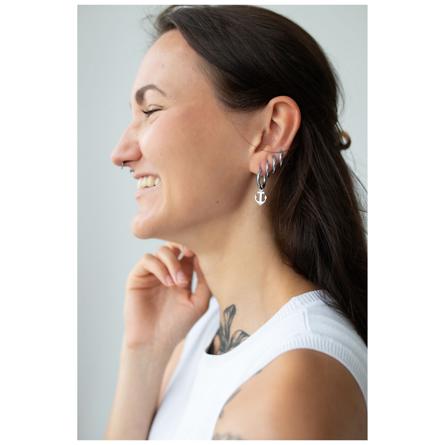 Femme avec boucles d'oreilles Little Anchor Hoops Femme aux longs cheveux noirs portant des boucles d'oreilles ancre en argent et souriant